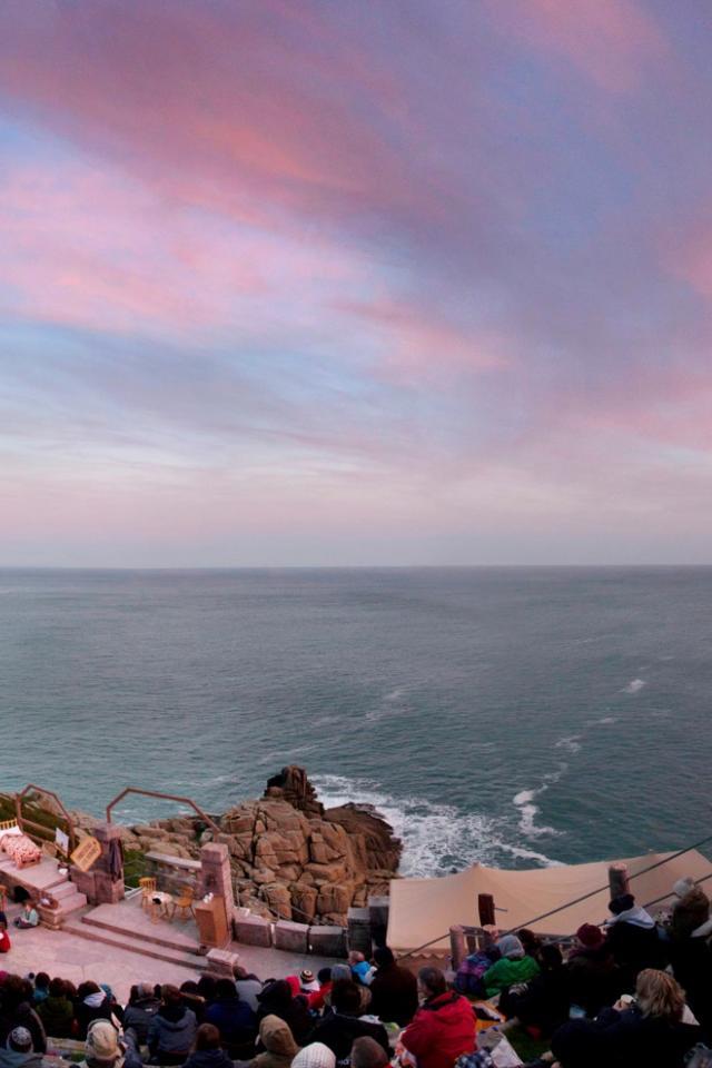 A sunset view of the Minack and Porthcurno bay. Audience enjoying a performance in the foreground