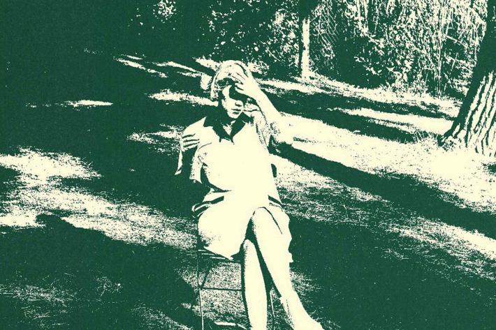Green tinted retro photograph of a young woman seated on a folding chair in the open air