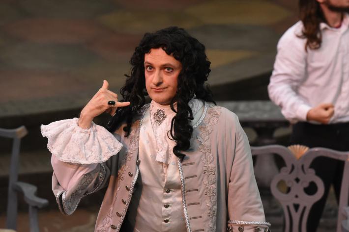 Actor in eighteenth century costume making a phone gesture with his hand