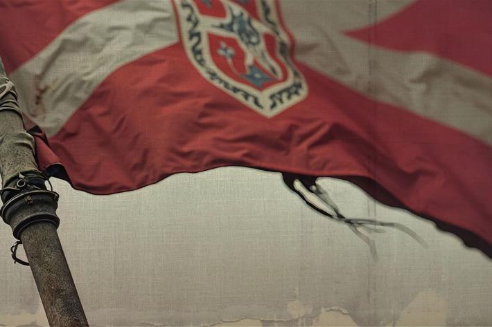 Close up of a tattered flag with a white St Andrew's cross on a red ground.