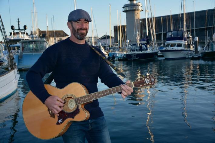 Will Keating with guitar on a keyside