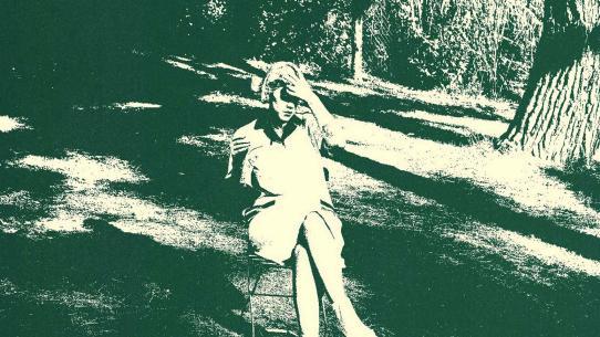 Green tinted retro photograph of a young woman seated on a folding chair in the open air